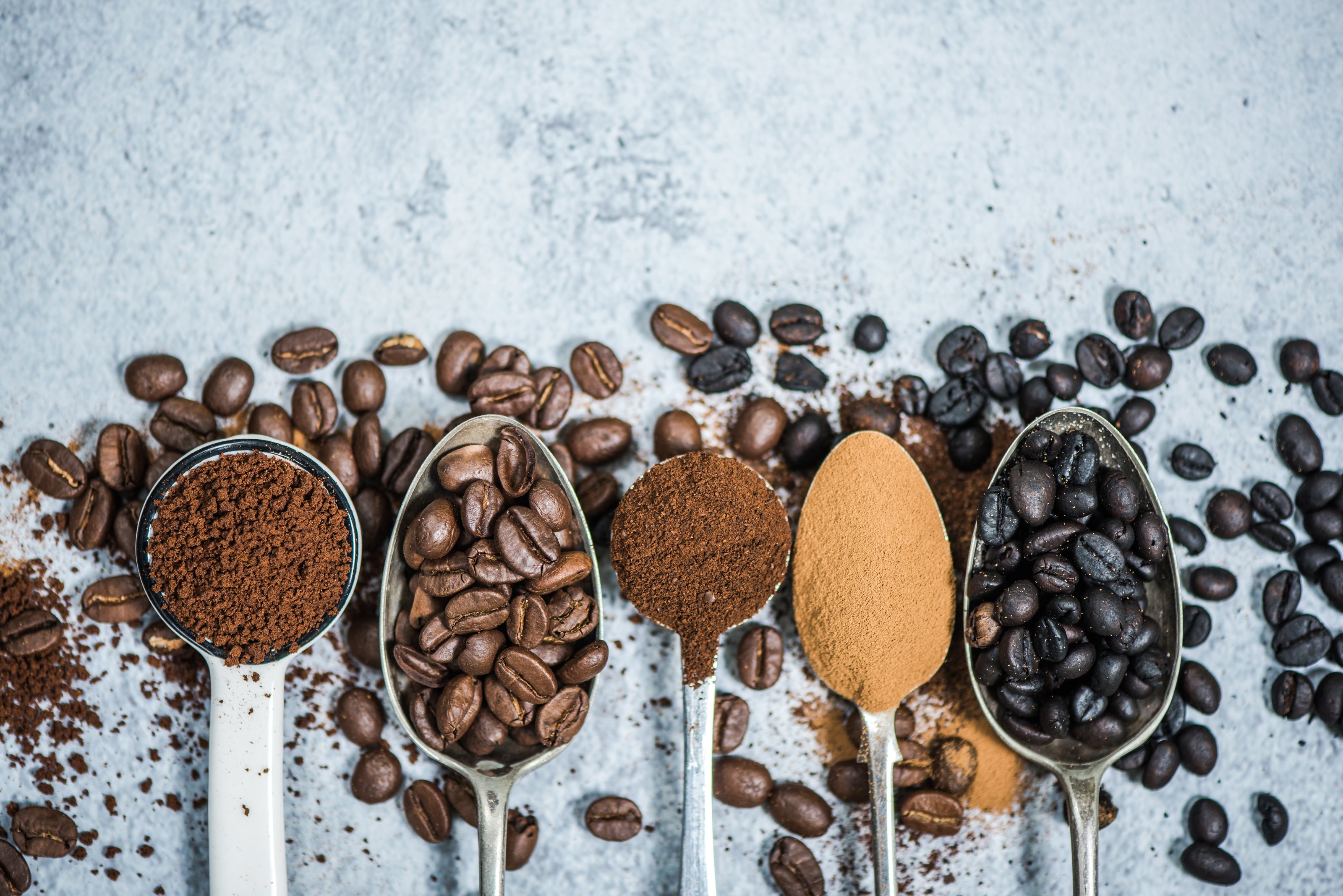 Spoons holding coffee beans and ground coffee at different roast levels